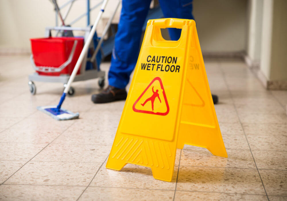 Caution wet floor sign with person mopping floor in the background