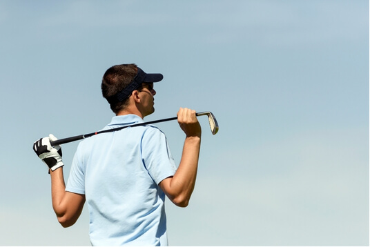 A golfer standing with a club resting across his shoulders, looking out onto the course, representing focus and readiness before the game.