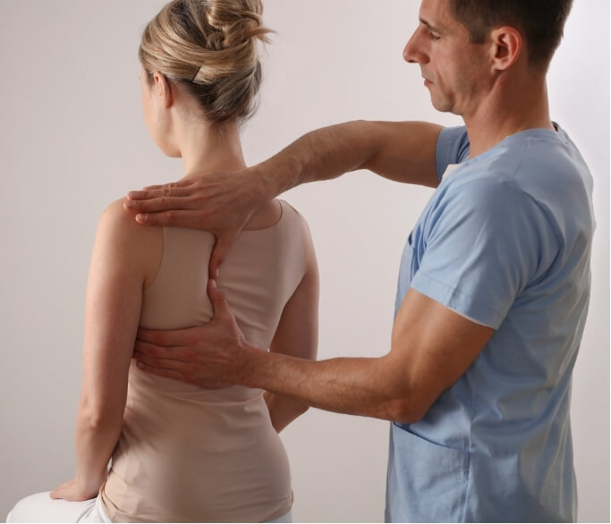 A physiotherapist assessing a woman’s thoracic and shoulder posture problem, demonstrating hands-on evaluation for postural imbalances and control issues.