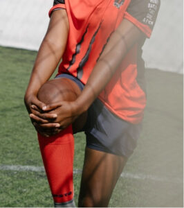 A touch football player in a red jersey holding their knee on the field, possibly indicating injury or muscle strain during a game.