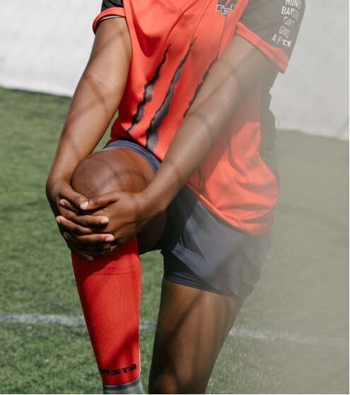 A touch football player in a red jersey holding their knee on the field, possibly indicating injury or muscle strain during a game.