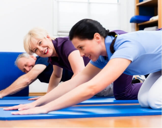 A group of older adults participating in a physiotherapist-led stretching or Pilates class on yoga mats, promoting mobility and joint-friendly exercise.