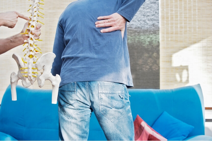 Man experiencing upper body discomfort as physiotherapist explains Thoracic Outlet Syndrome with spine model.