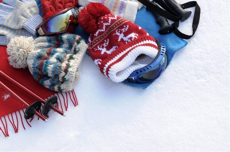 Winter gear including hats, scarves, and goggles laid out on snow, representing preparation for winter sports and preventing winter sports injuries.