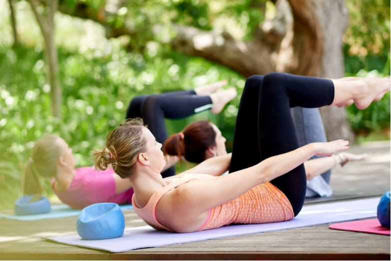 Group of women doing pilates-based core exercises for lower back pain outdoors on yoga mats.