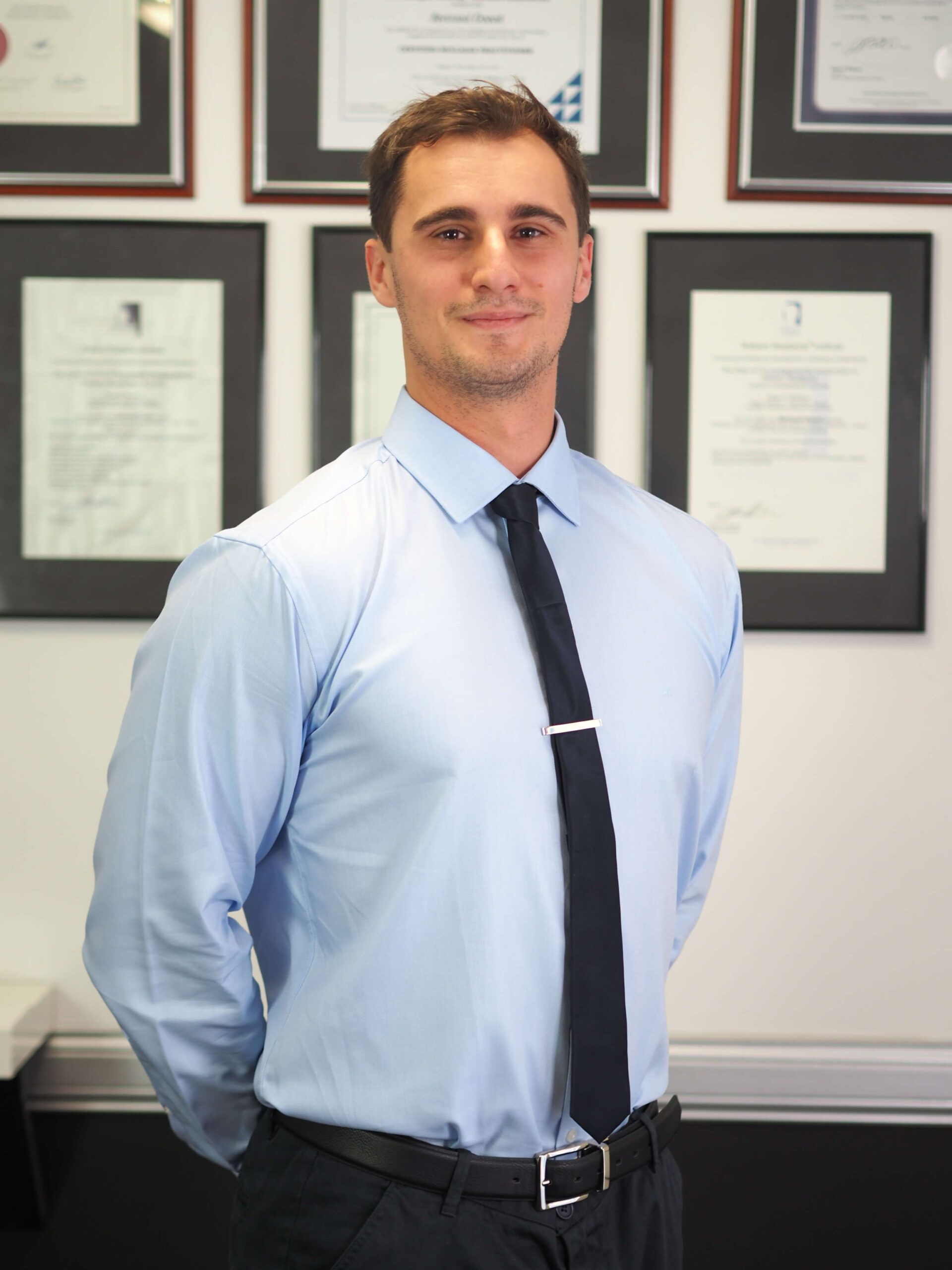 Matt Ivan, M Physio Gold Coast clinician, standing in front of framed physiotherapy qualifications