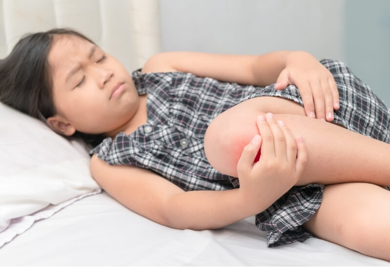 Girl lying down holding her painful, inflamed knee – common symptom of Osgood-Schlatter disease.