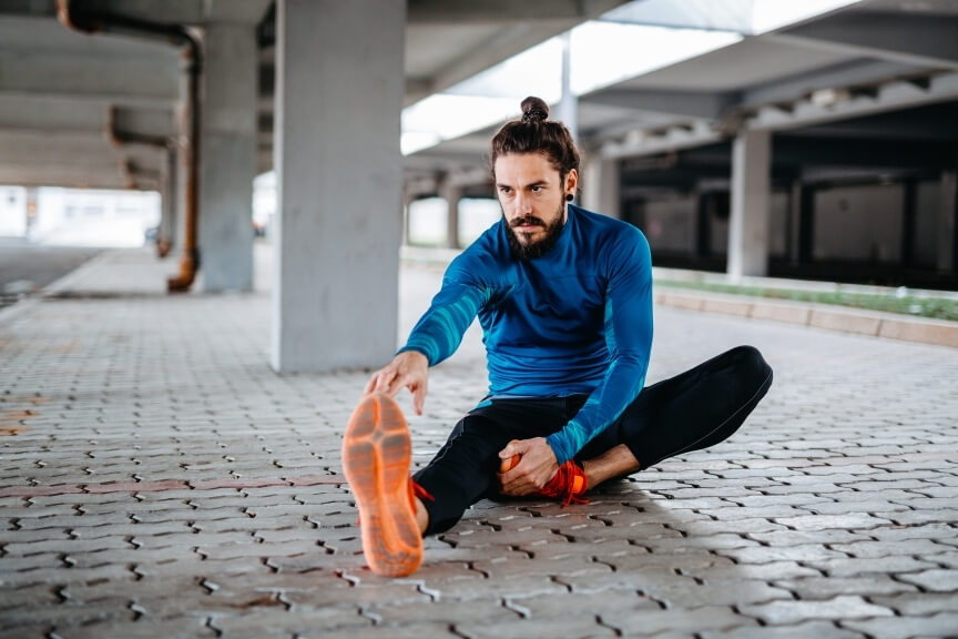 Athlete stretching hamstrings to relieve muscle tightness causes related to load and recovery