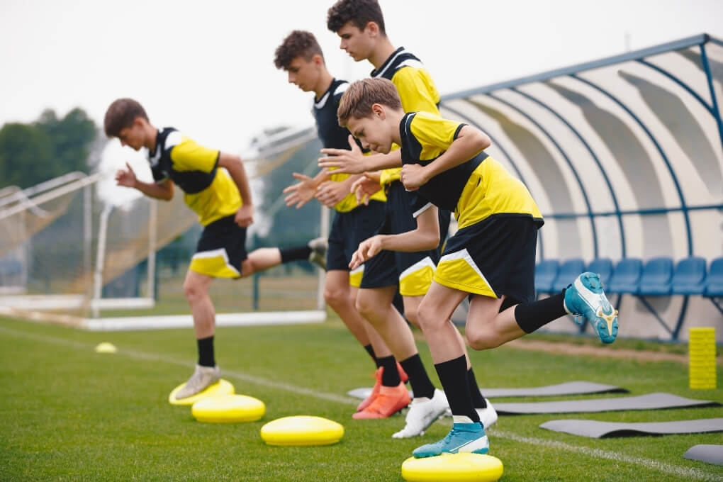 Young football players completing balance and running drills as part of a purposeful exercise program.