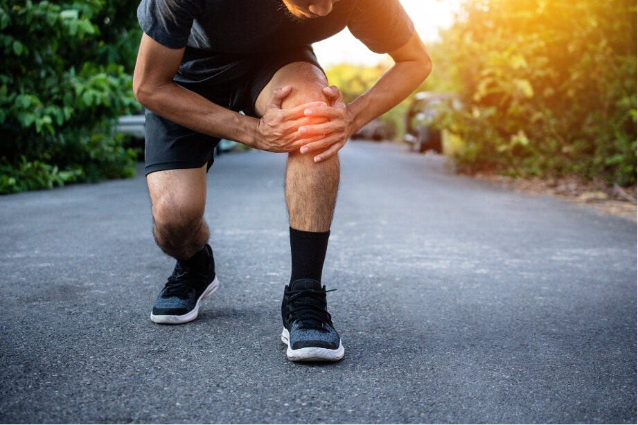 Runner holding his knee while experiencing pain during exercise outdoors, highlighting the decision to exercise through pain.