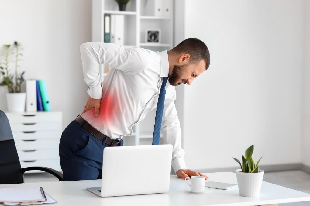 Office worker holding his lower back in pain after experiencing a workplace injury.