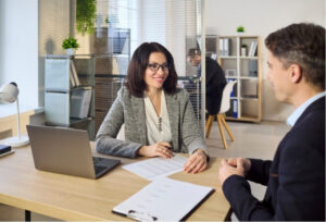 Woman speaking with a man across an office desk about work, representing communication and planning after a workplace injury.