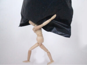 Wooden mannequin carrying a large black load overhead, representing progressive loading and the body’s capacity to manage physical demands.