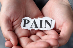 Two hands holding a piece of paper displaying the word “PAIN”, representing pain perception and the experience of pain.