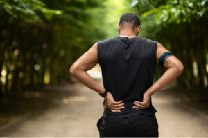 Man standing outdoors with his hands on his lower back, illustrating concerns about spinal alignment and back pain.